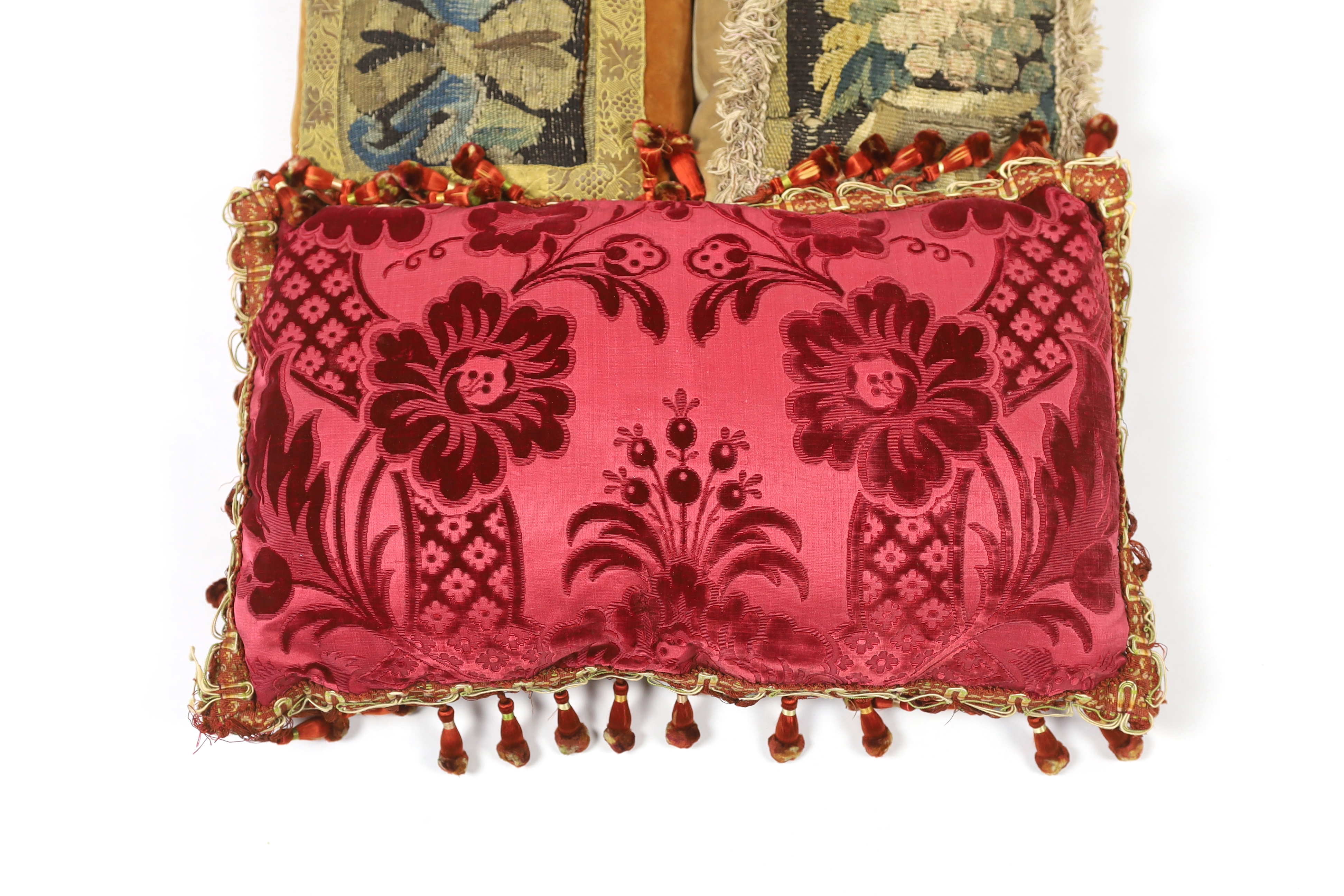 Two late 18th century Flemish verdure tapestry fragments made into cushions, plus a 19th century French Aubusson and an early 19th century Italian burgundy cut velvet damask panel, both made into cushions, all trimmed wi